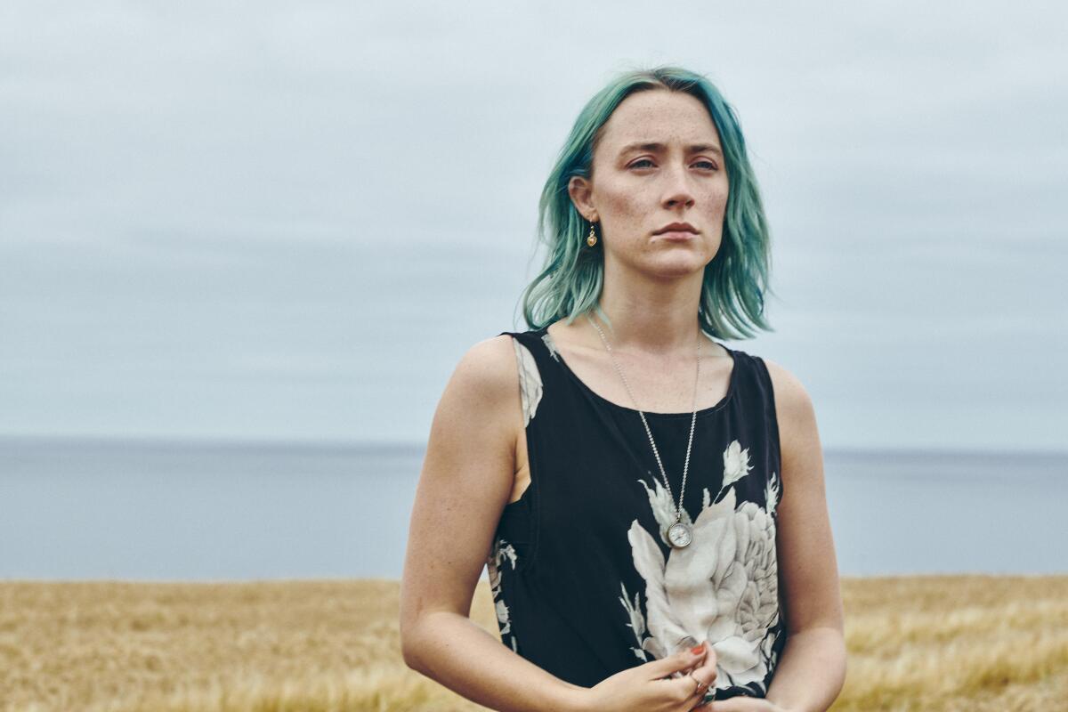 A woman with dyed-green hair stands on a beach.