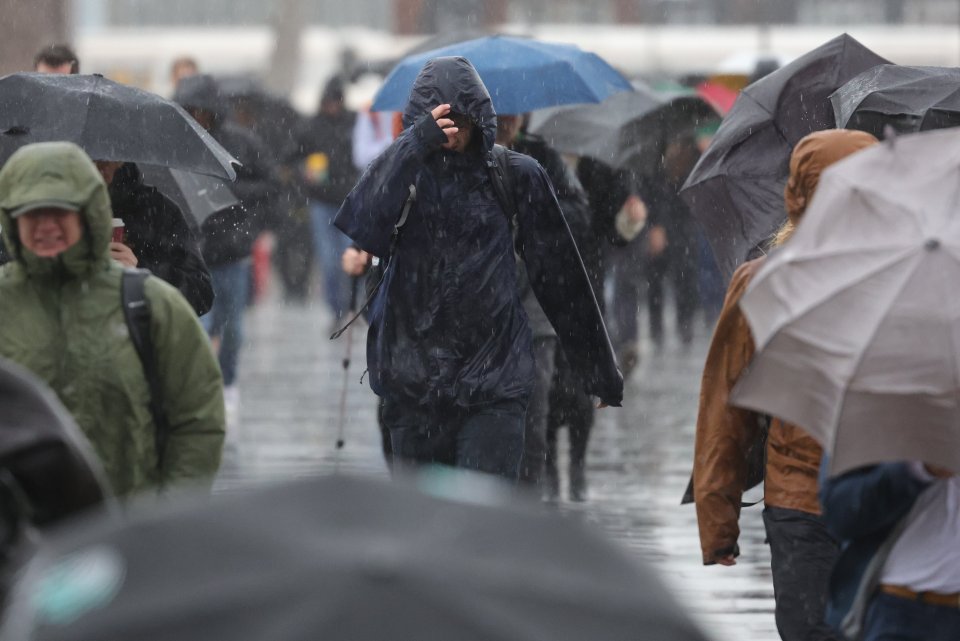 Commuters attempt to shelter as they cross London Bridge during torrential rain