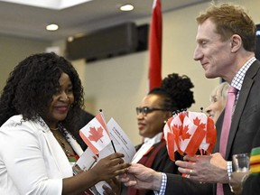 Cladice Awatia Tsafack receives a Canadian flag from Minister of Immigration, Refugees and Citizenship Marc Miller, left, after becoming a Canadian citizen during a citizenship ceremony in Ottawa, on Wednesday, Feb. 28, 2024.