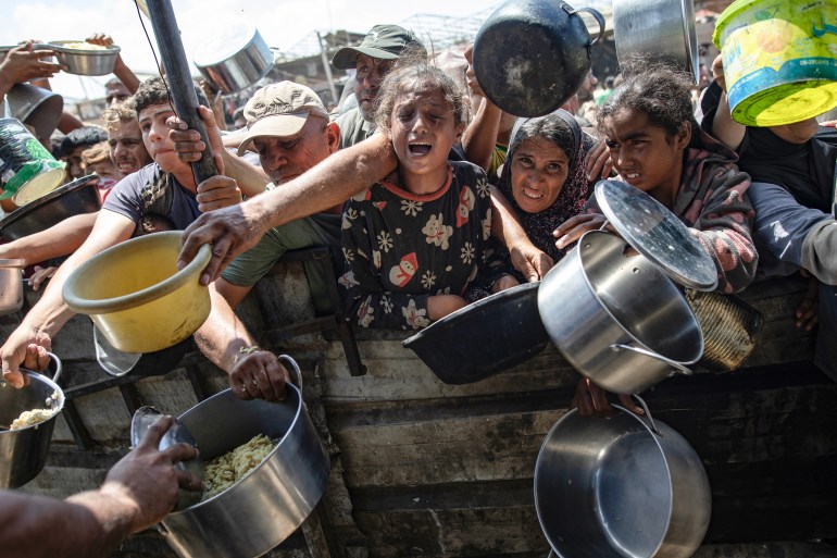 Internally displaced Palestinians receive food donated by a charity, in Khan Younis