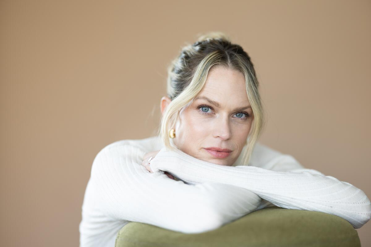 A woman in a white turtleneck lays her head on her crossed arms