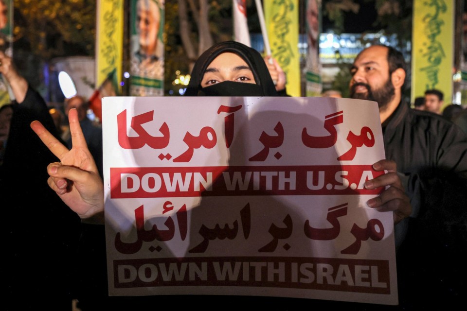 An Iranian woman holds up a sign reading 'Down with USA. Down with Israel' at a protest march