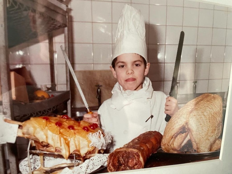 Simon as a boy in chef whites holding two knives