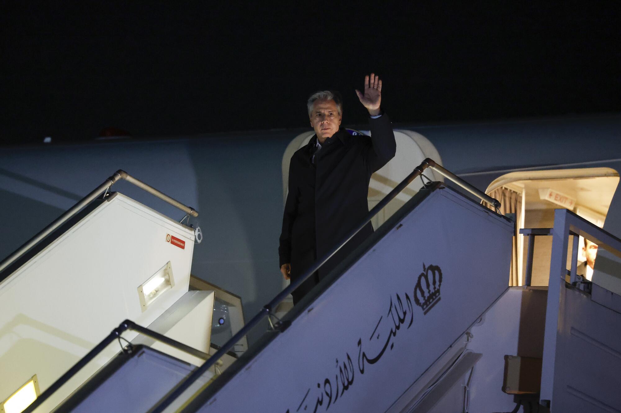 A man in a dark coat waves while descending the steps as he disembarks from an aircraft