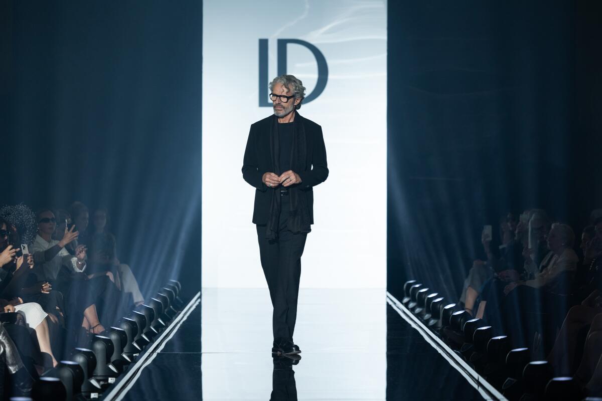 A man dressed in all black walks down the runway at a fashion show.