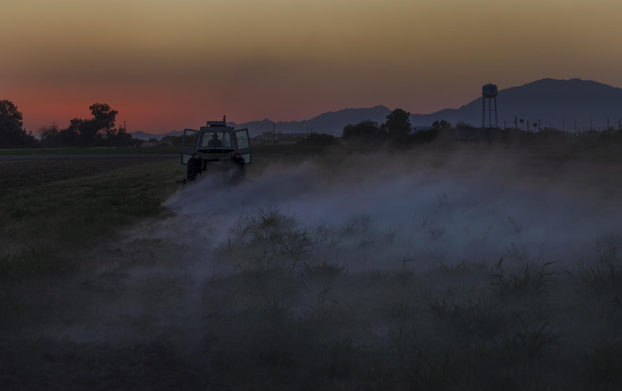 A farmer drives his tractor to turn the soil as dusk falls over the desert landscape in the Gila River Indian Community.