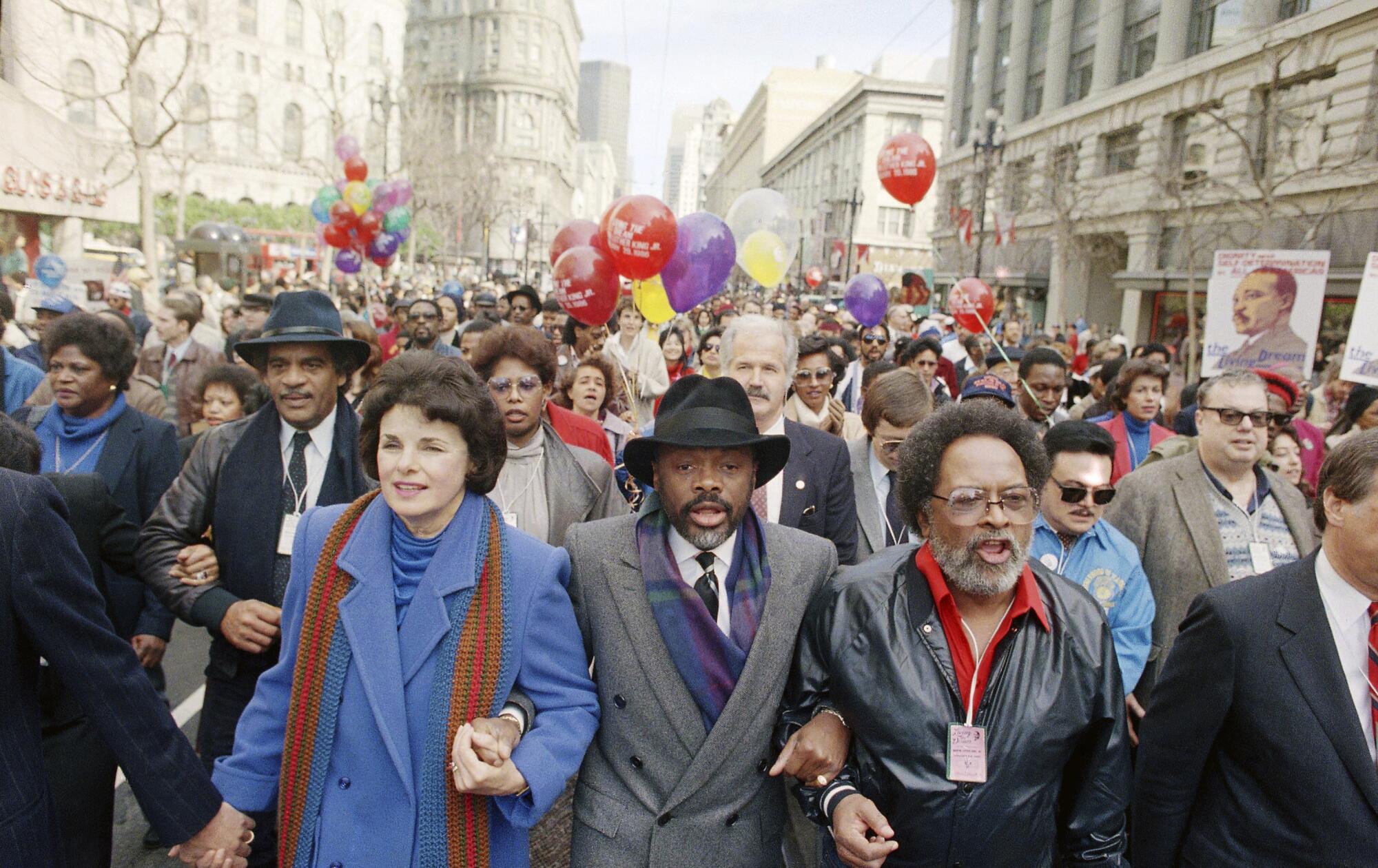 Dianne Feinstein, Willie Brown and the Rev. Cecil Williams hold hands during a march with a crowd following them.