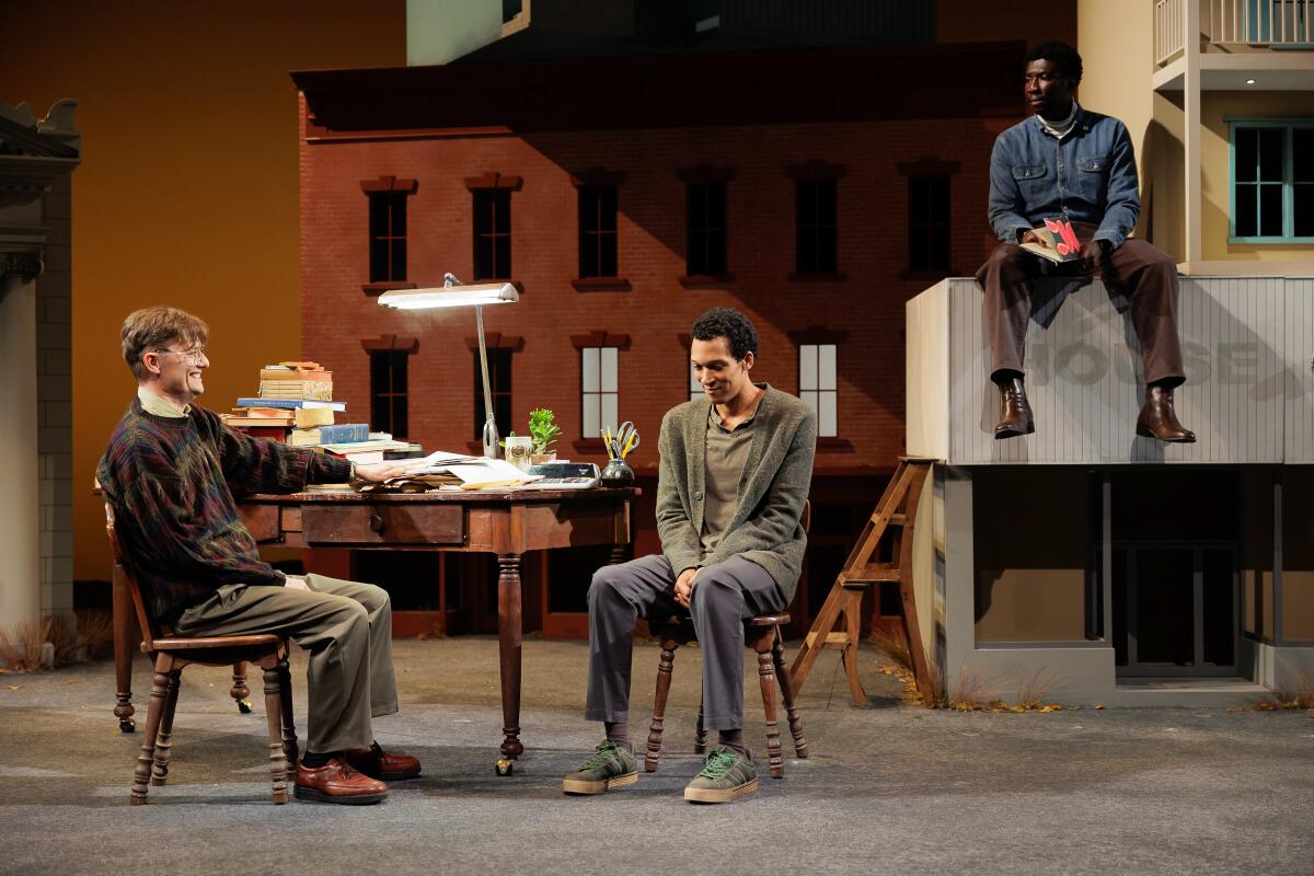 Two men sit at a desk, observed by another man on a ledge in the play "Primary Trust."