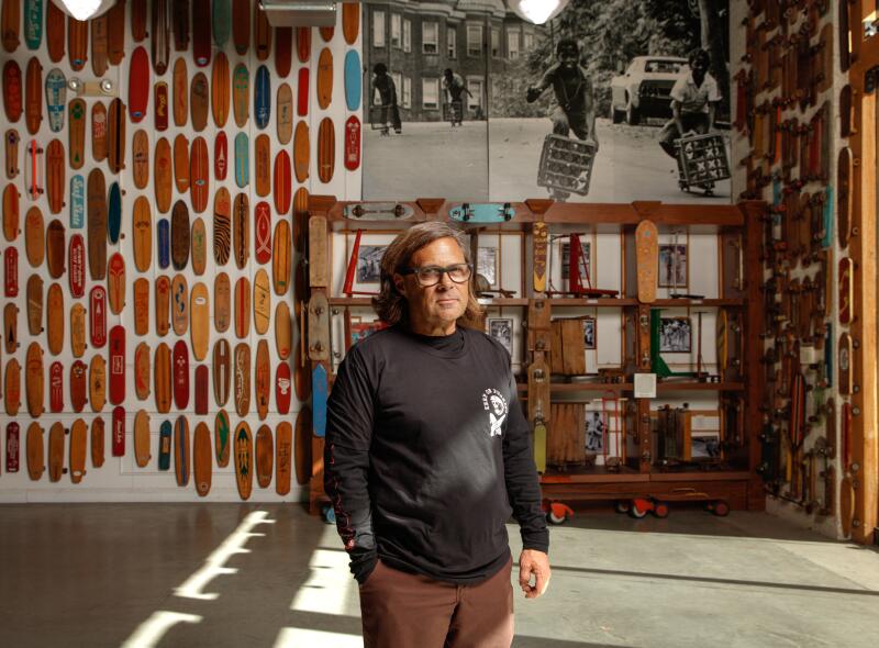 A person stands in a room with many skateboards on the walls.