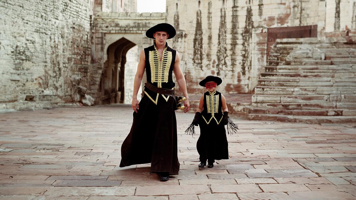 A man and a child in bullfighting costumes walk down a dusty street.