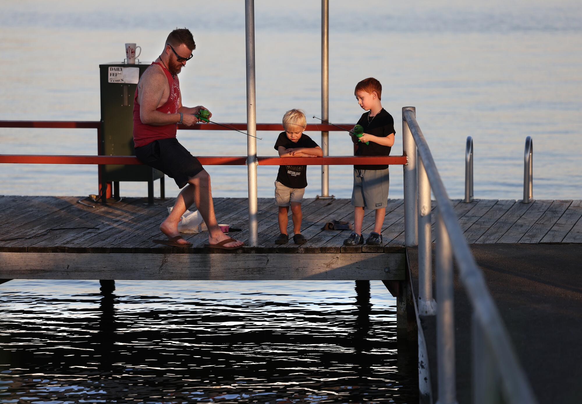 A man and young boy fish using small fishing poles while a younger boy watches 