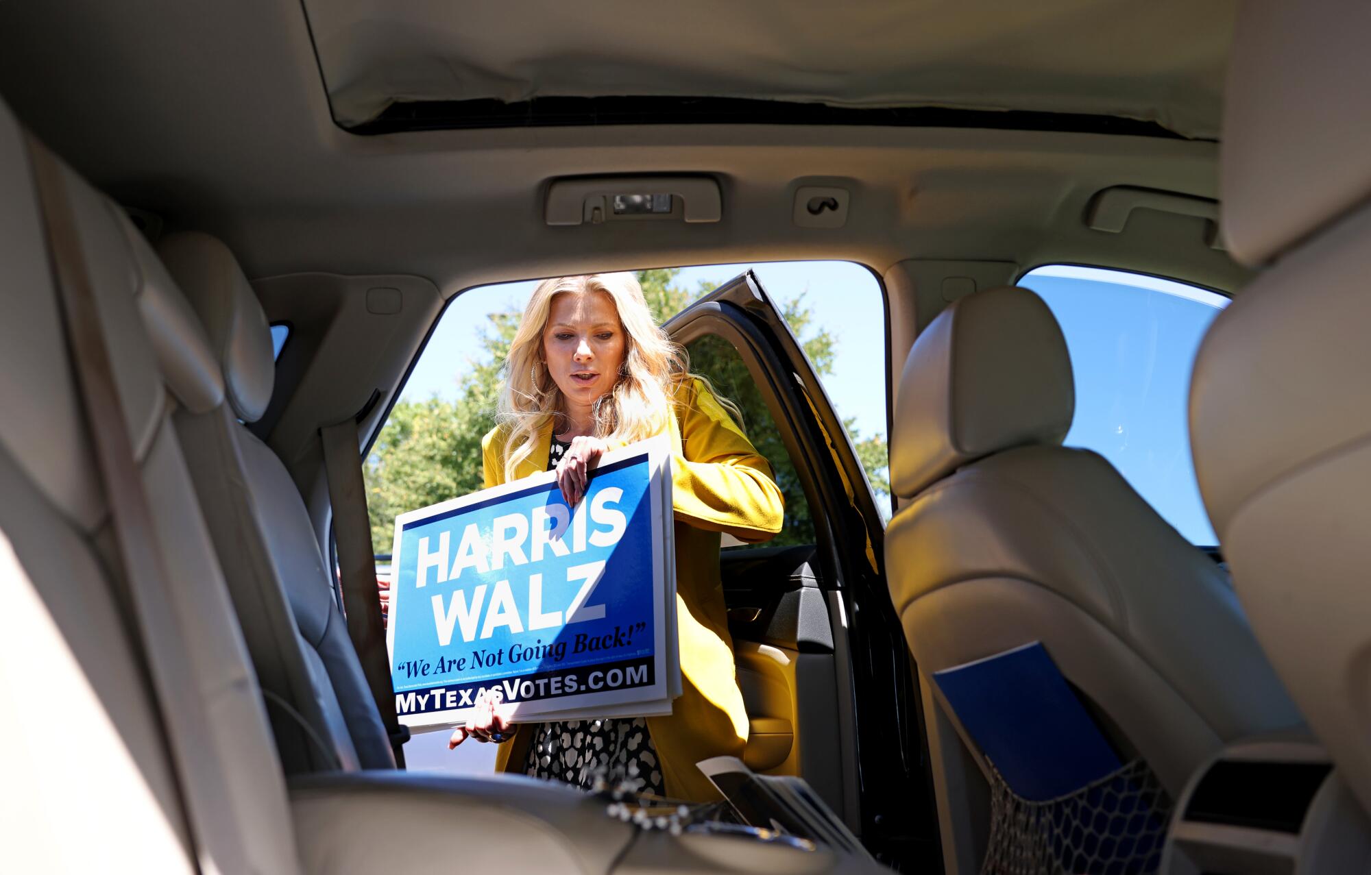 A woman holds Harris-Walz campaign signs next to a  vehicle 