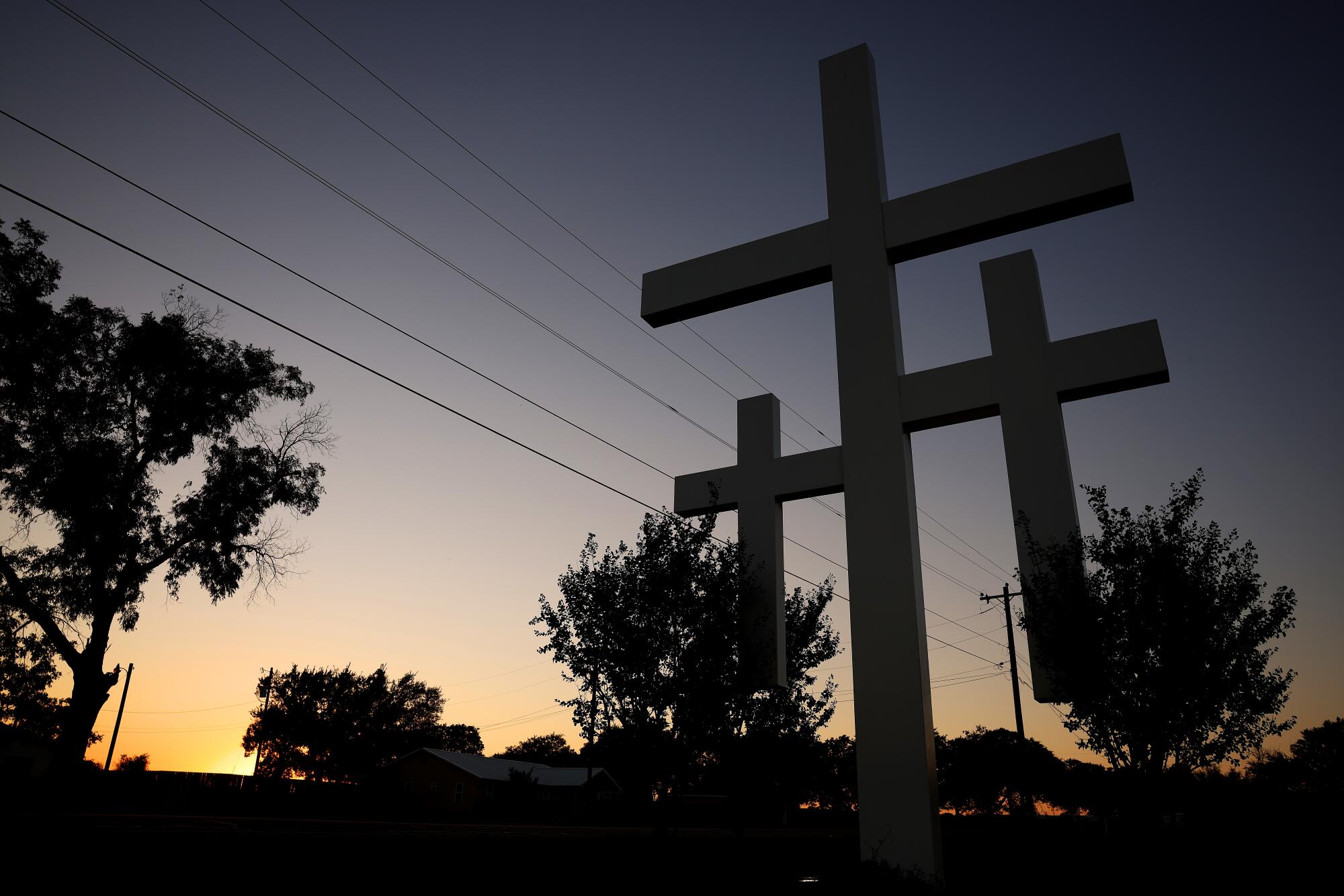 The sun sets behind a set of three crosses 