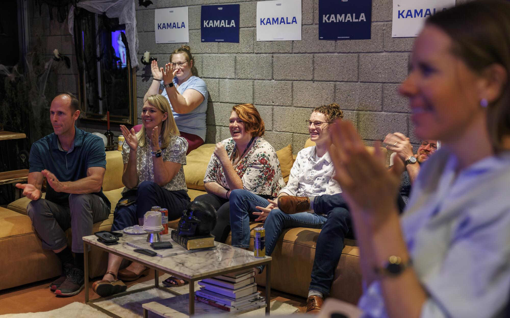 Several people applaud while watching the vice presidential debate.