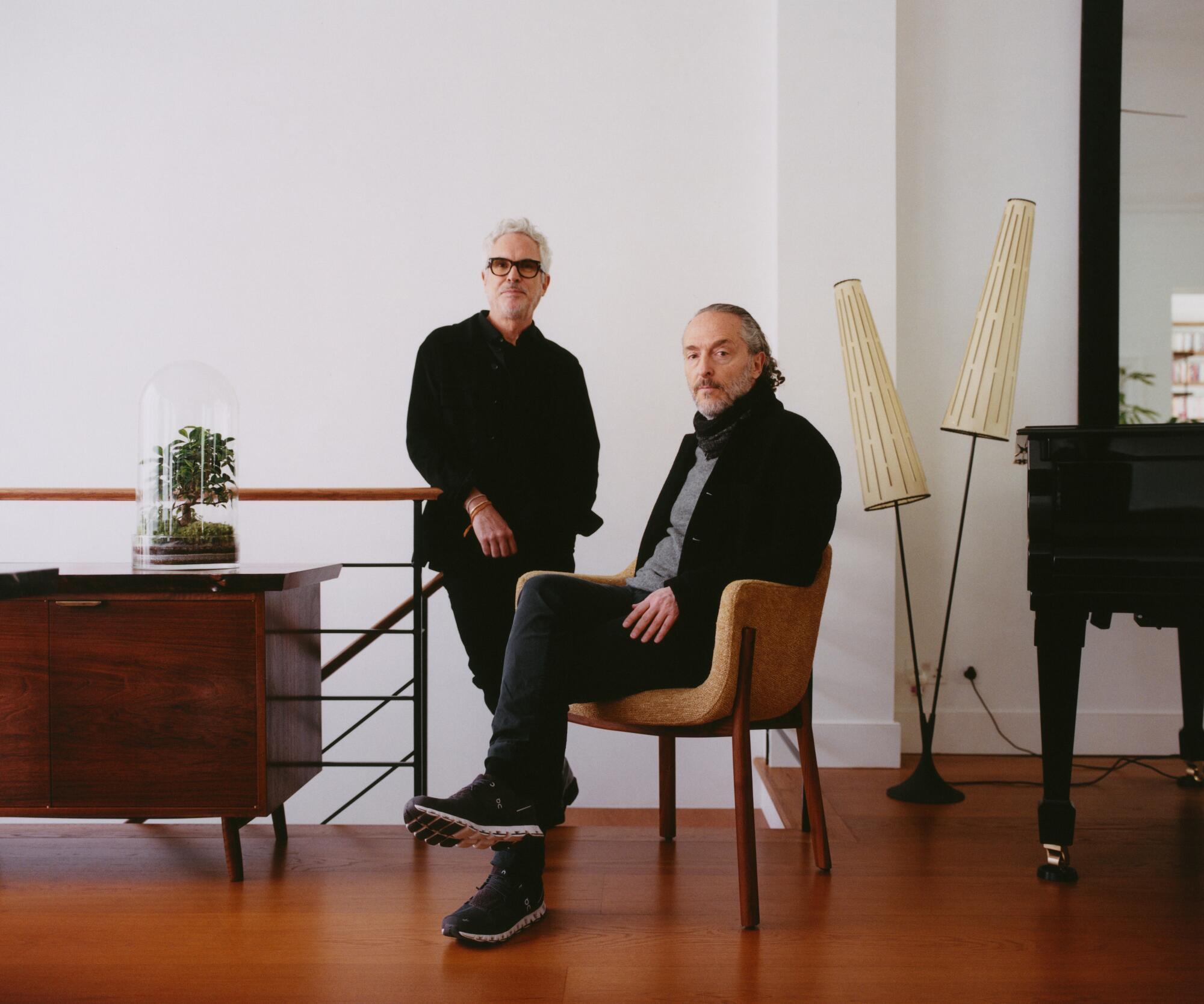 Director Alfonso Cuarón stands at the top of stairs next to a seated Emmanuel Lubezki, his cinematographer, in a modern room