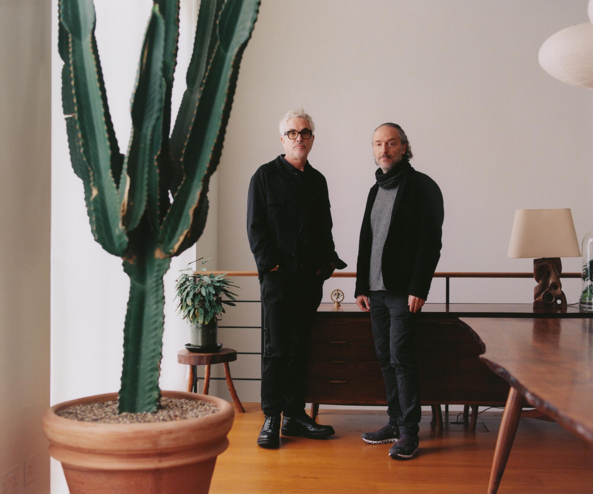 Director Alfonso Cuaron stands in a modern room with cinematographer Emmanuel Luzbeki and a large potted cactus.