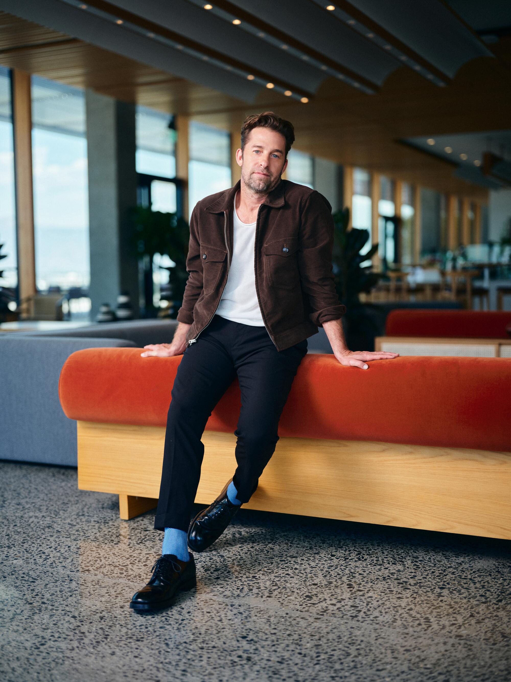  A man leans against an orange and yellow couch