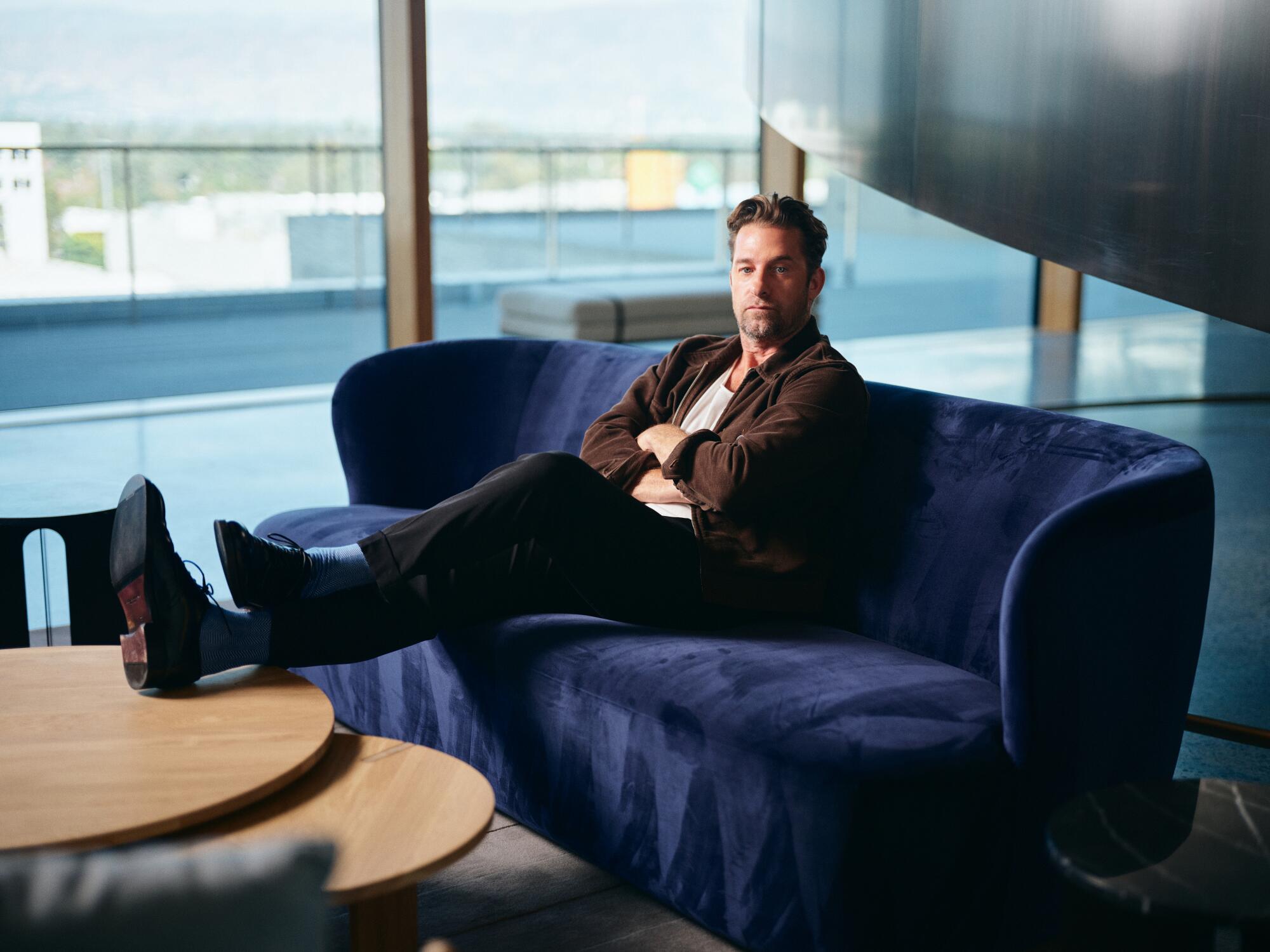 A man sits on a blue couch with his feet resting on a nearby coffee table