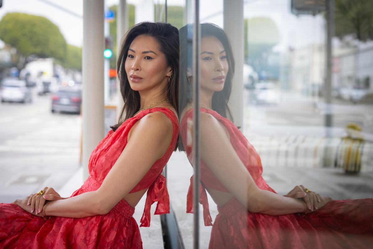 A seated woman in a pink dress leaning back against her reflection in a window.