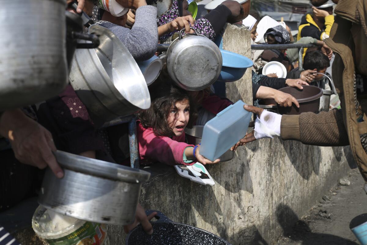 Palestinians line up for food holding pots and other containers