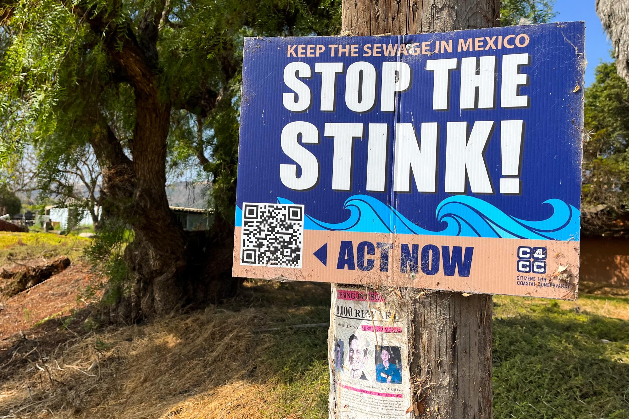 A blue sign on a tree trunk reads: Keep the sewage in Mexico: Stop the Stink!