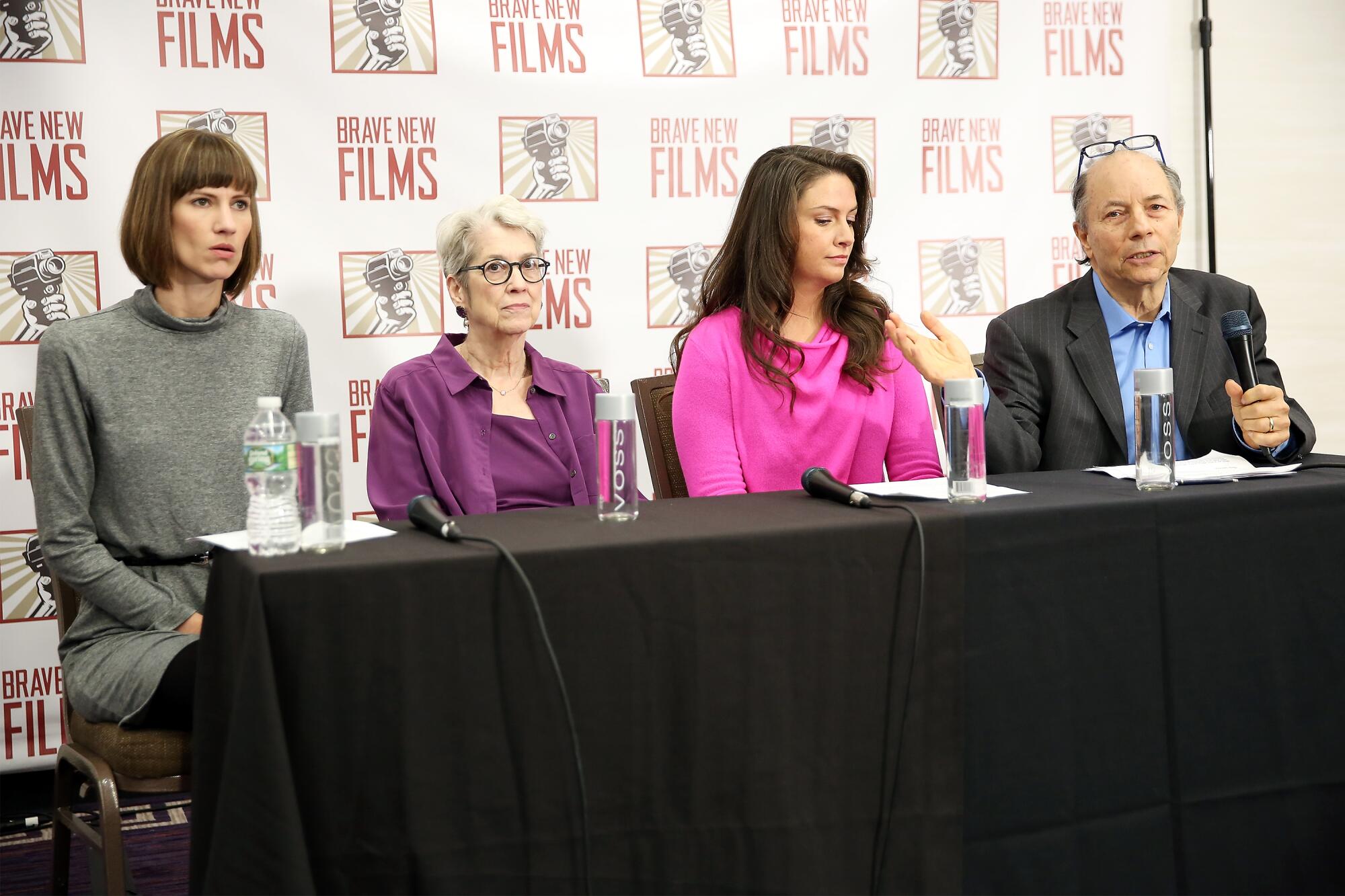 Three women and a man sit in a row at a news conference