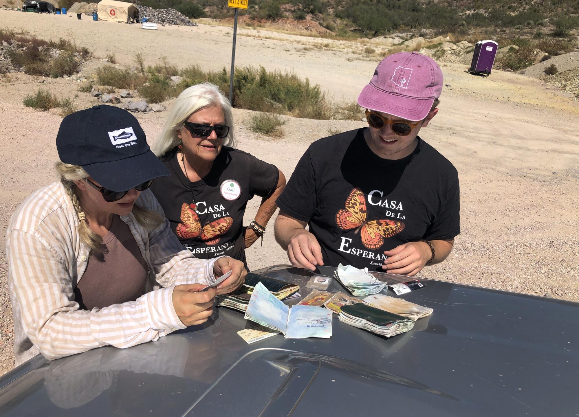 A blond woman is flanked by two people looking at documents on the hood of a vehicle