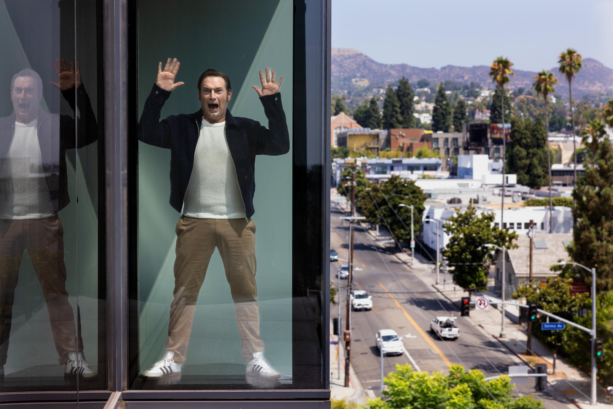 A man in a dark jacket, white T-shirt and khaki pants is seen screaming through a glass wall.