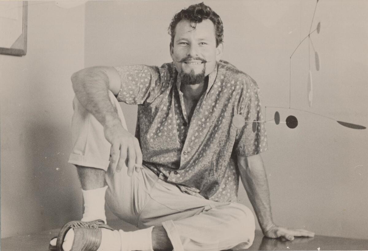 A young goateed man in an open-collared shirt and sandals.