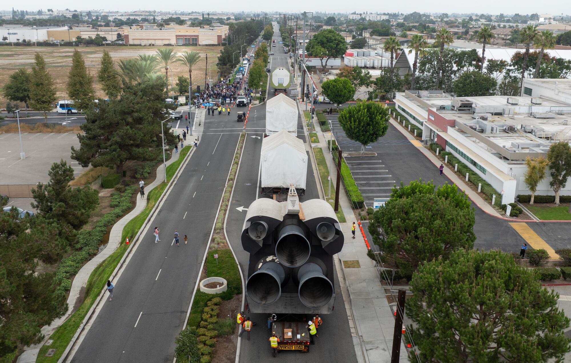 An aerial view of a space shuttle model being trucked along a city street.