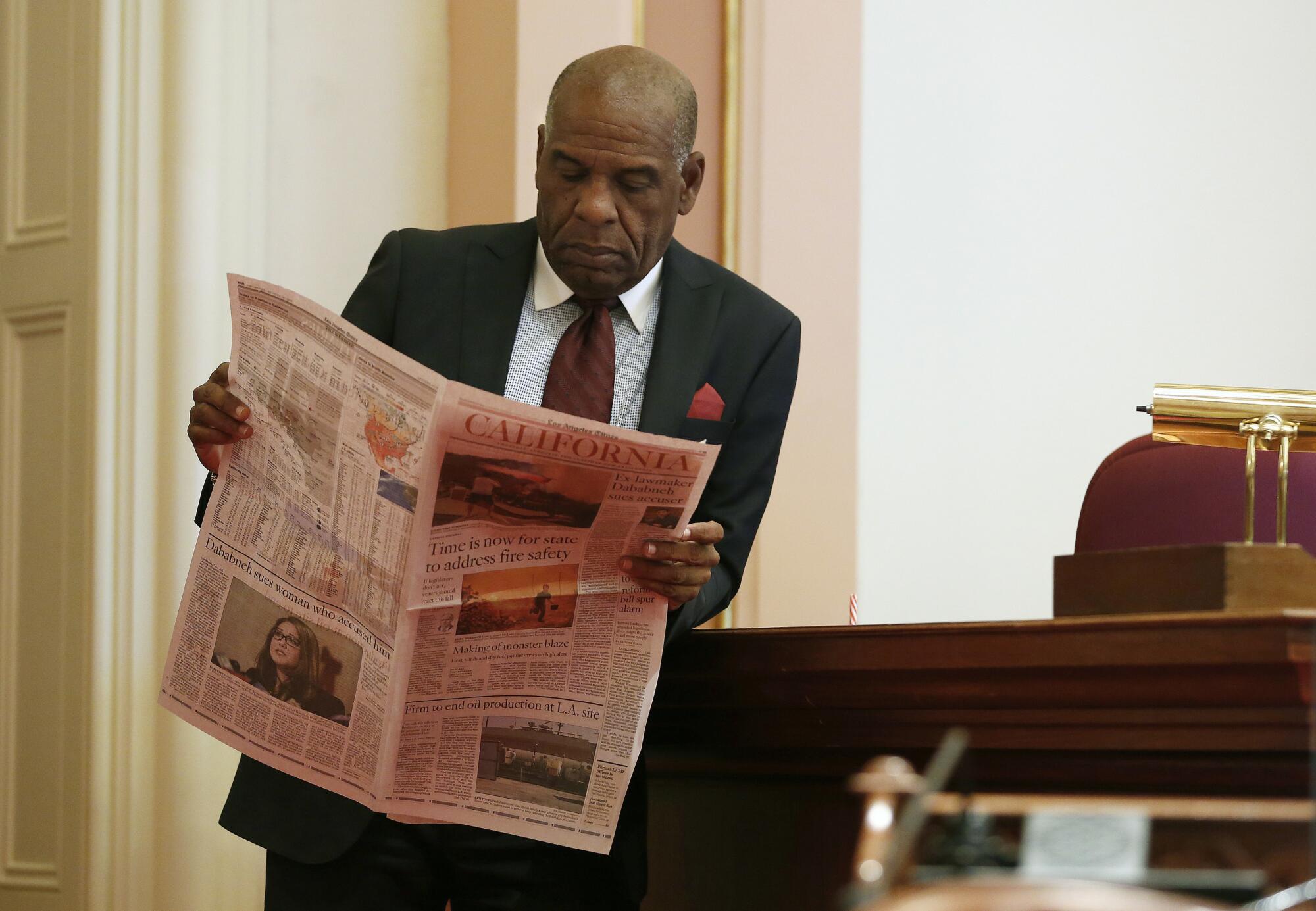 California State Sen. Steve Bradford wearing a suit and reading the L.A. Times