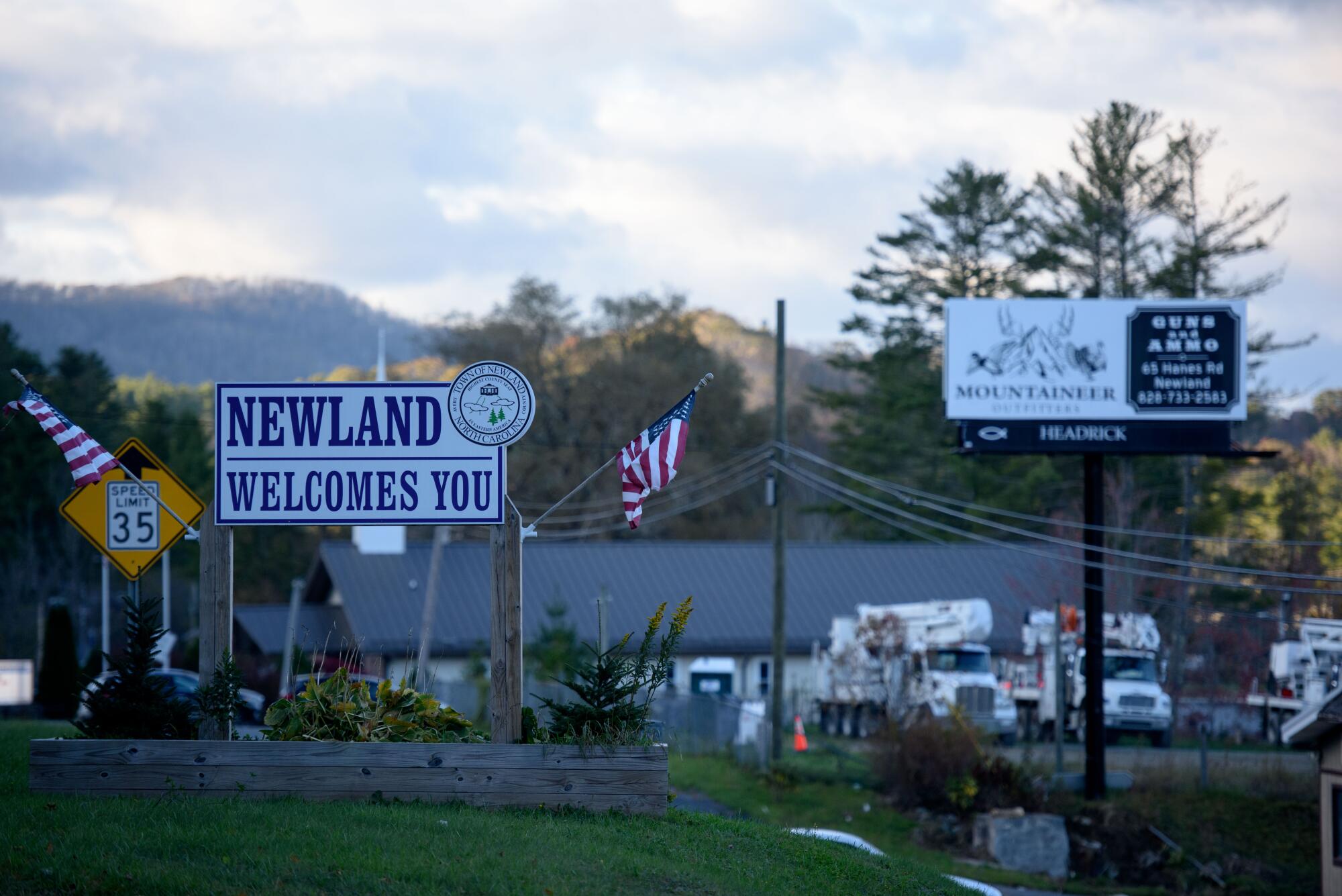 A welcome sign for Newland, N.C., with utility trucks and an advertisement for guns and ammunition in the background. 