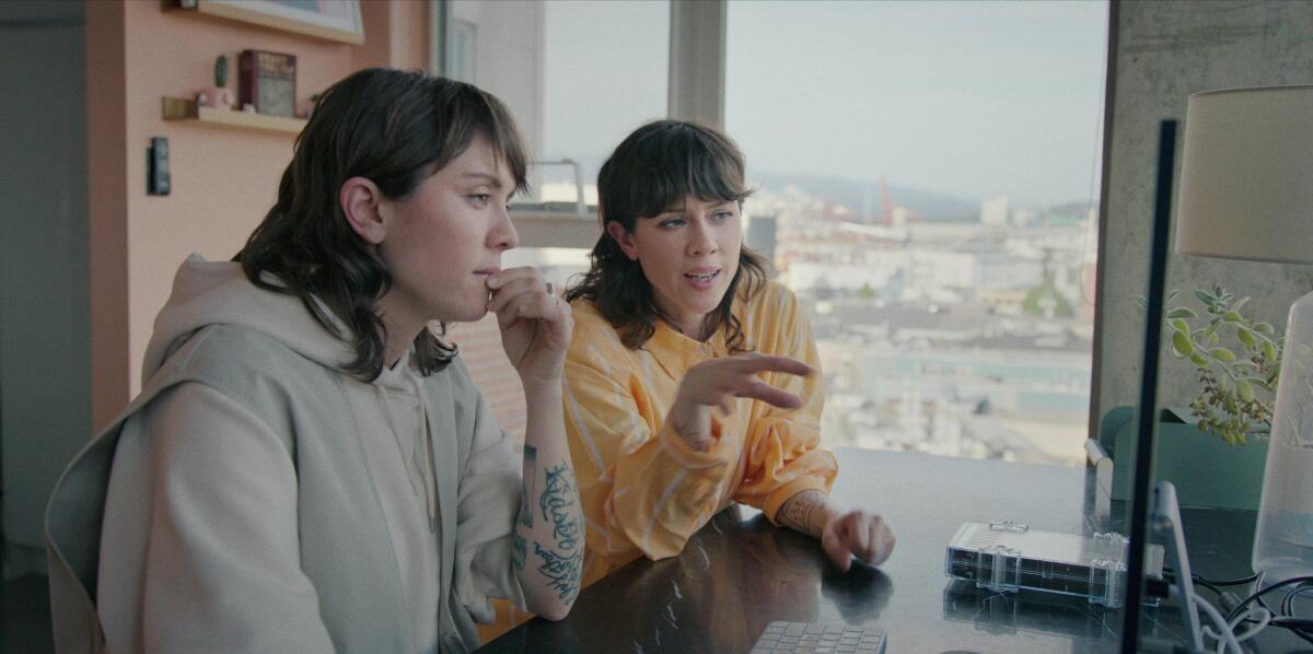 Twin siblings Tegan and Sara Quin sit at a desk before a computer monitor.