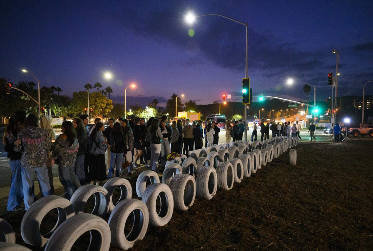 People stand next to dozens of white tires at a roadside memorial.