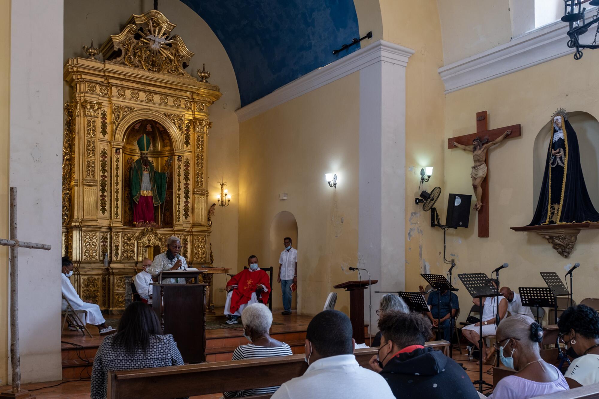 People attending a service in a church with an ornate altar backdrop, a crucifix and other religious figures