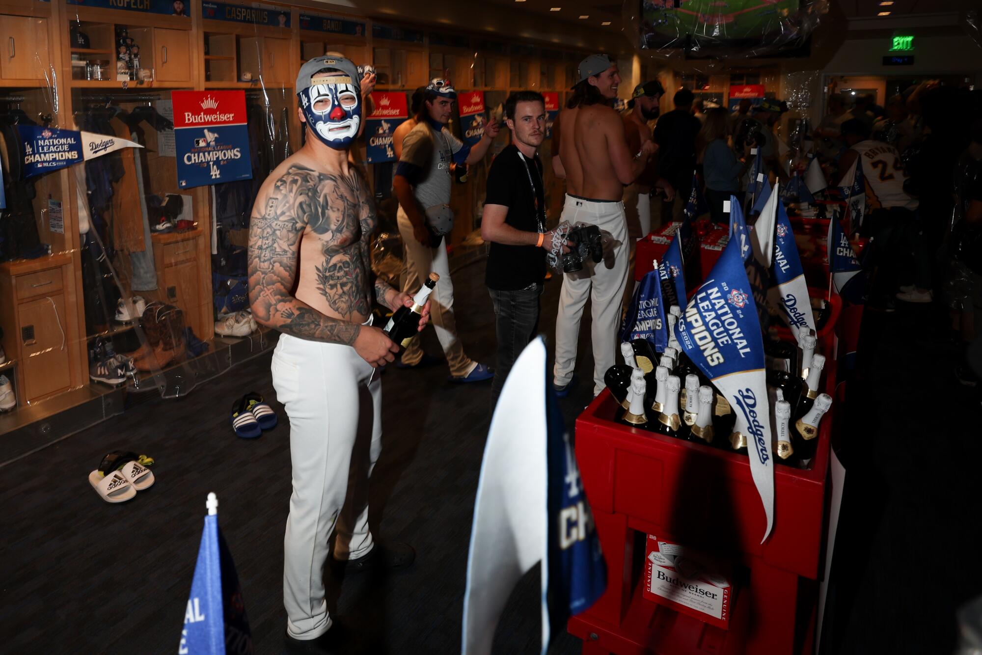 A shirtless Anthony Banda dons a clown mask while holding a champagne bottle in the locker room