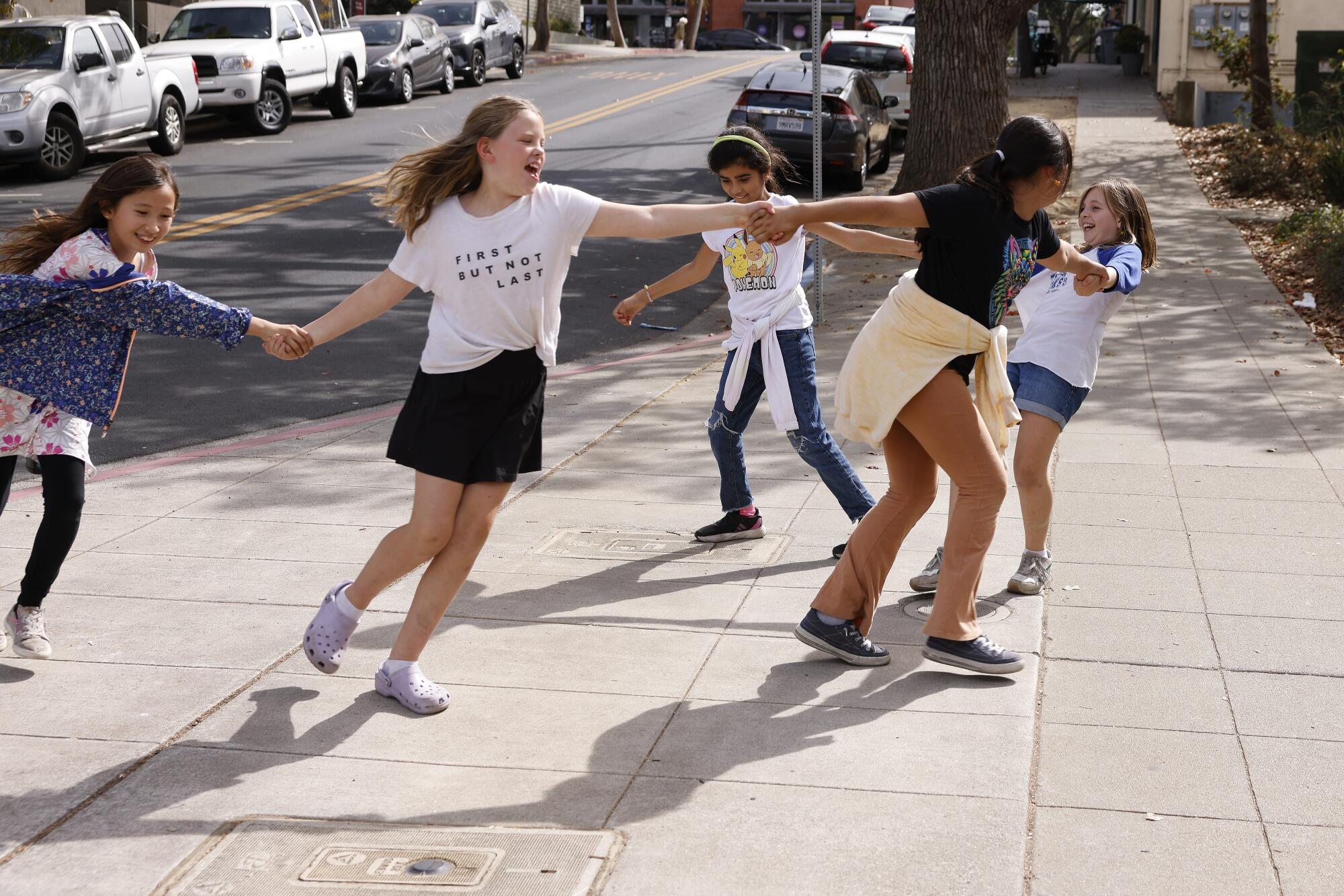 Schoolgirls holding hands and casting their shadows as they weave along a sidewalk by their elementary campus