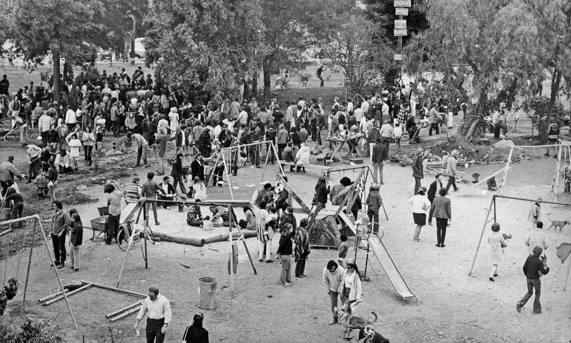 A black-and-white photo of dozens of people doing work on a park and playing on slides and swings assembled on the ground