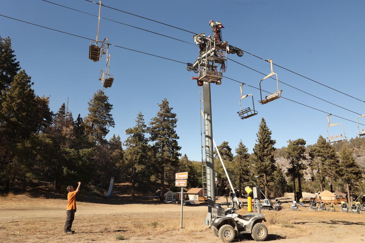 A worker in an orange shirt stands near chair lifts at a ski resort where it hasn't snowed yet