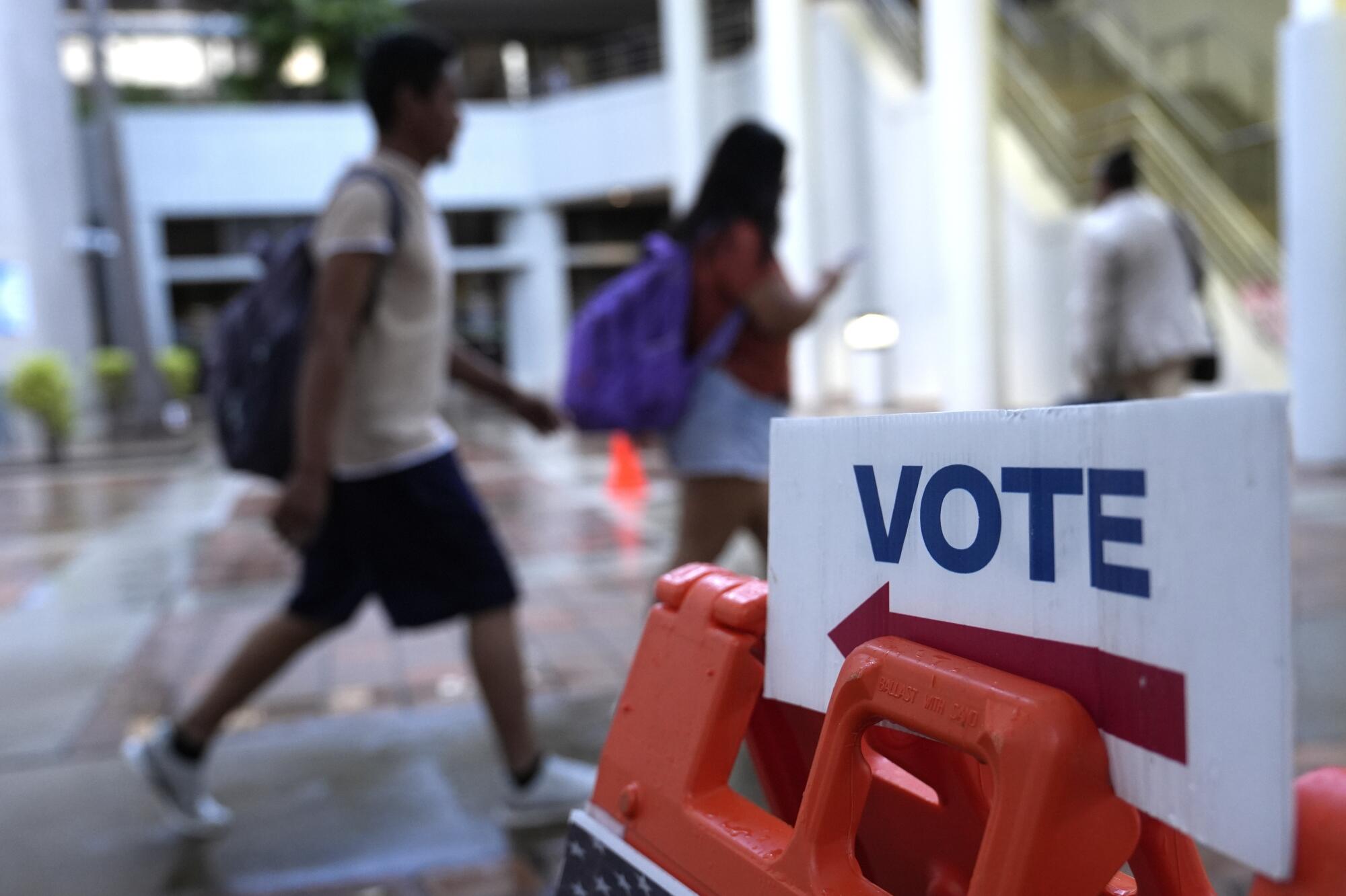 People walk past a vote sign in Miami