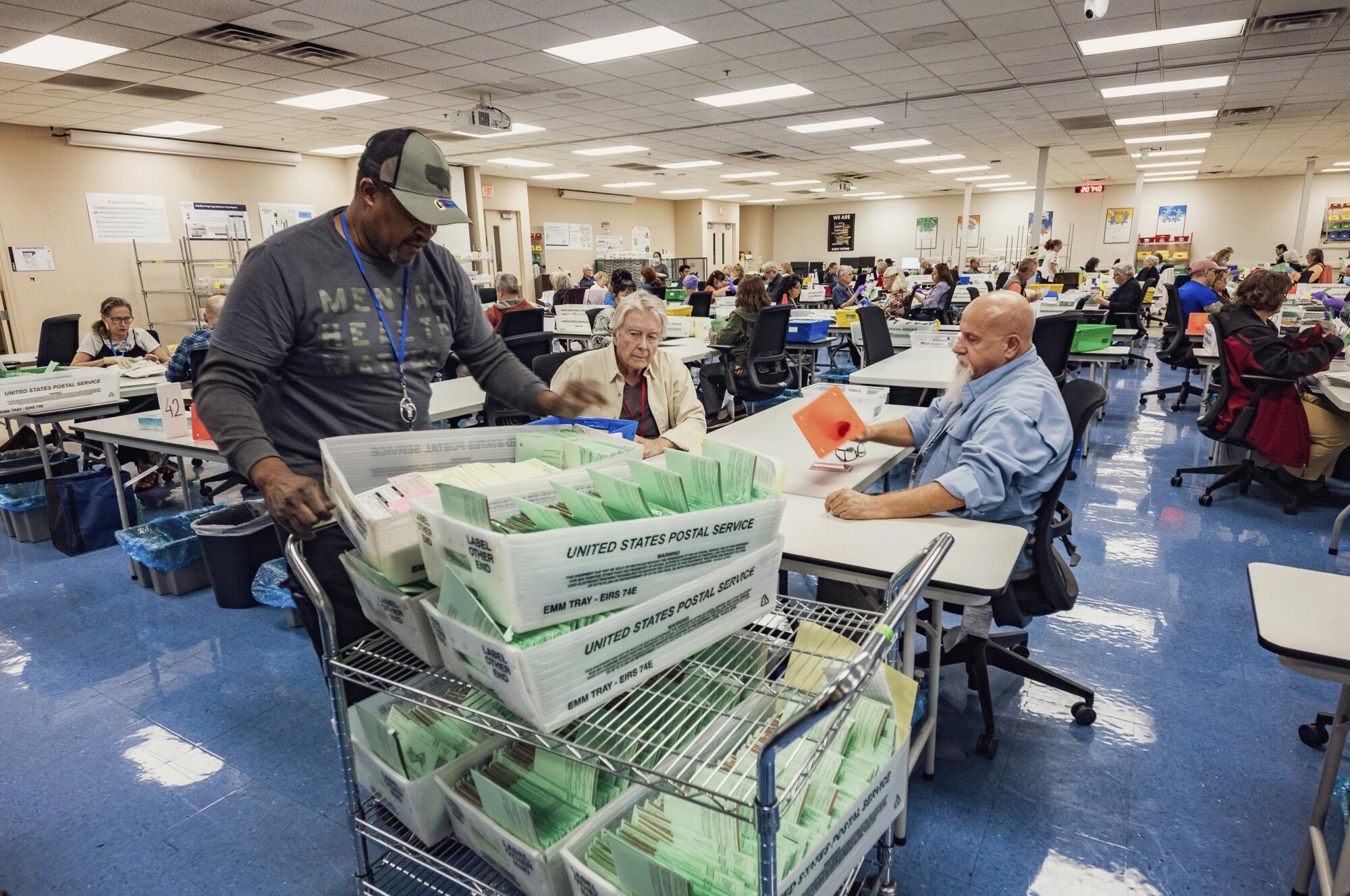 Election workers open envelopes and sort ballots in an auditorium