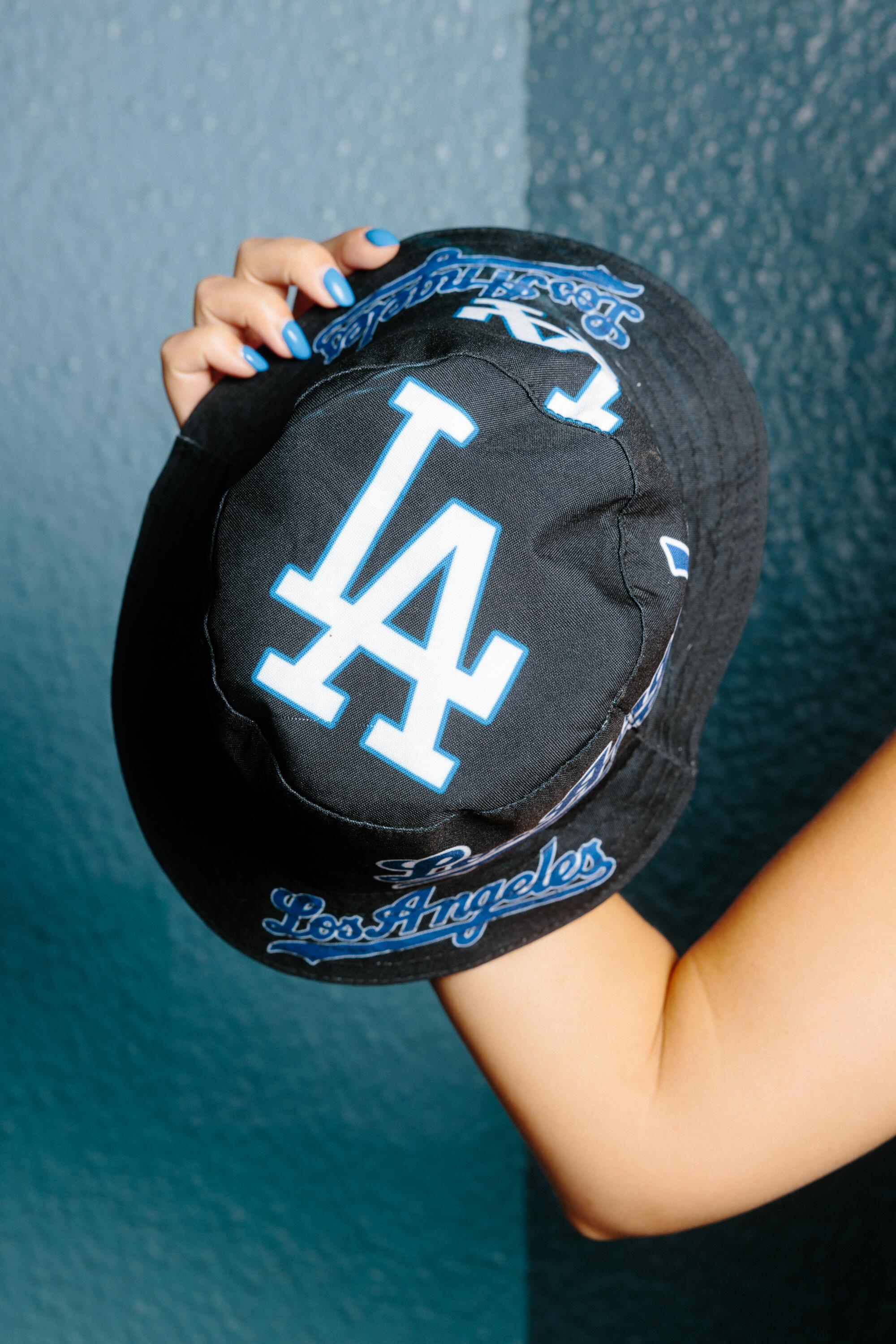 A hand holds a black, blue and white Dodgers hat with a brim.