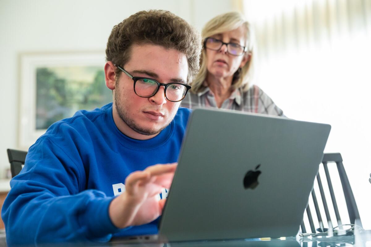 A teenage boy on his laptop as a woman looks over her shoulder.