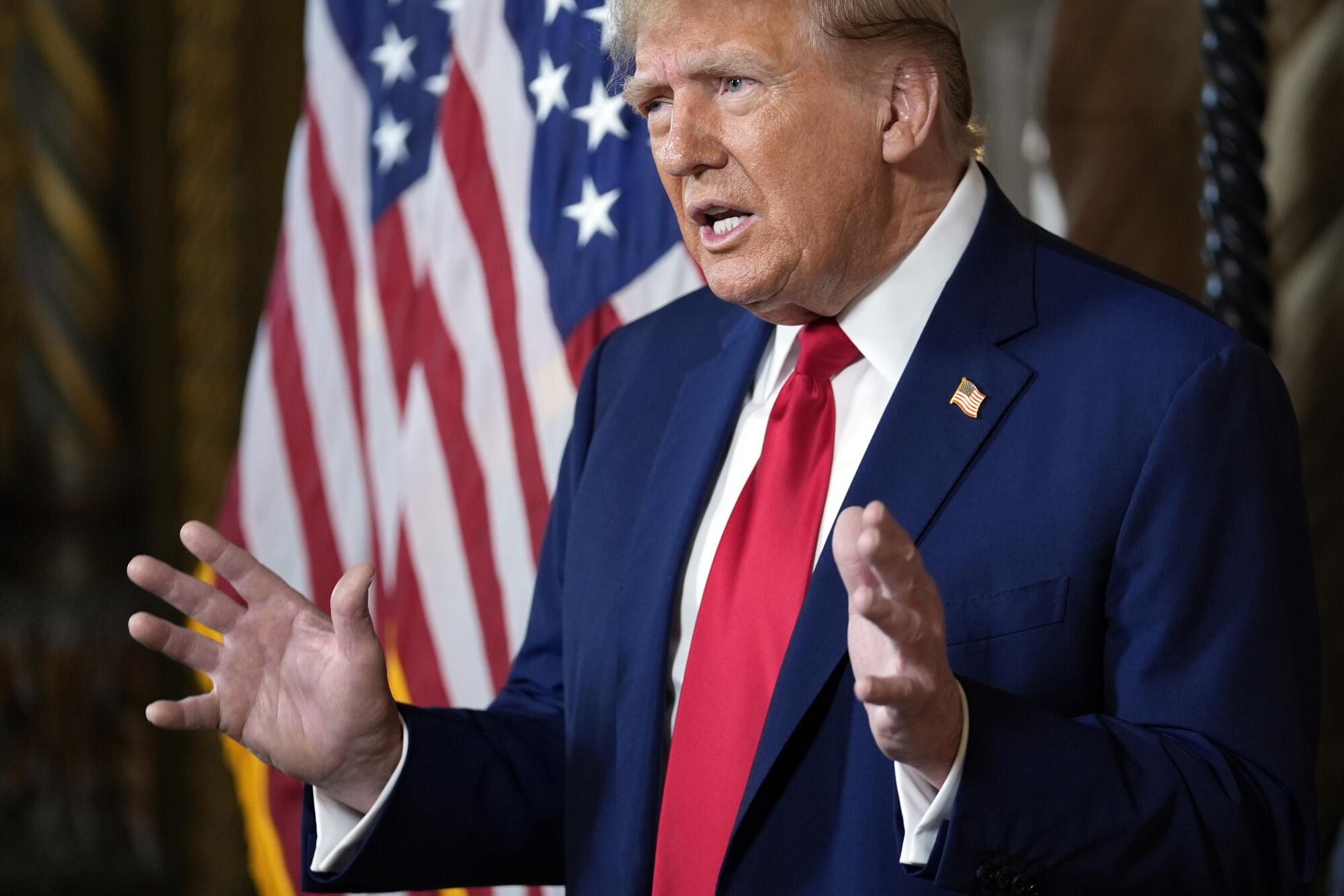 Donald Trump gestures as he speaks with flags in the background