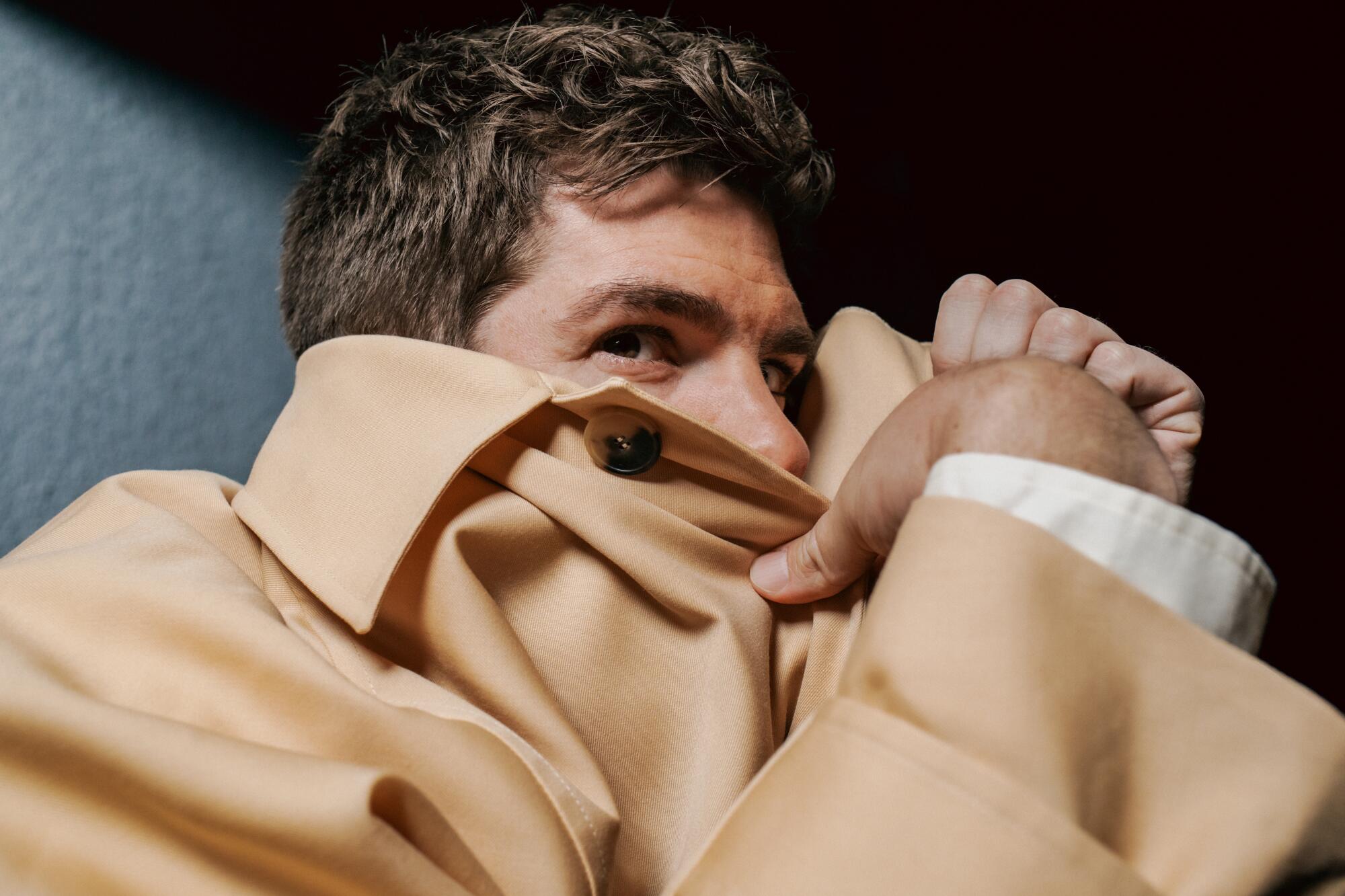 Andrew Garfield hides the lower half of his face under a large beige coat