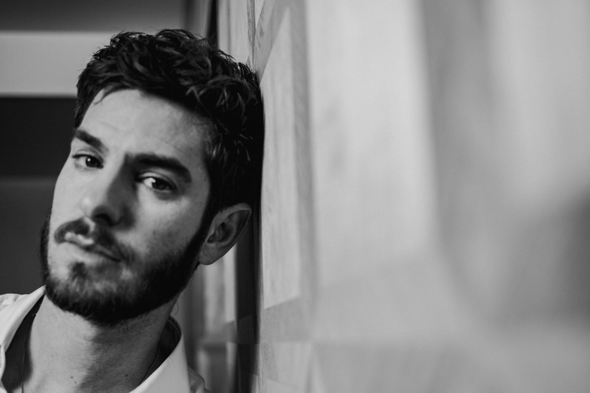 A black-and-white photo of Andrew Garfield leaning his head against a wall.