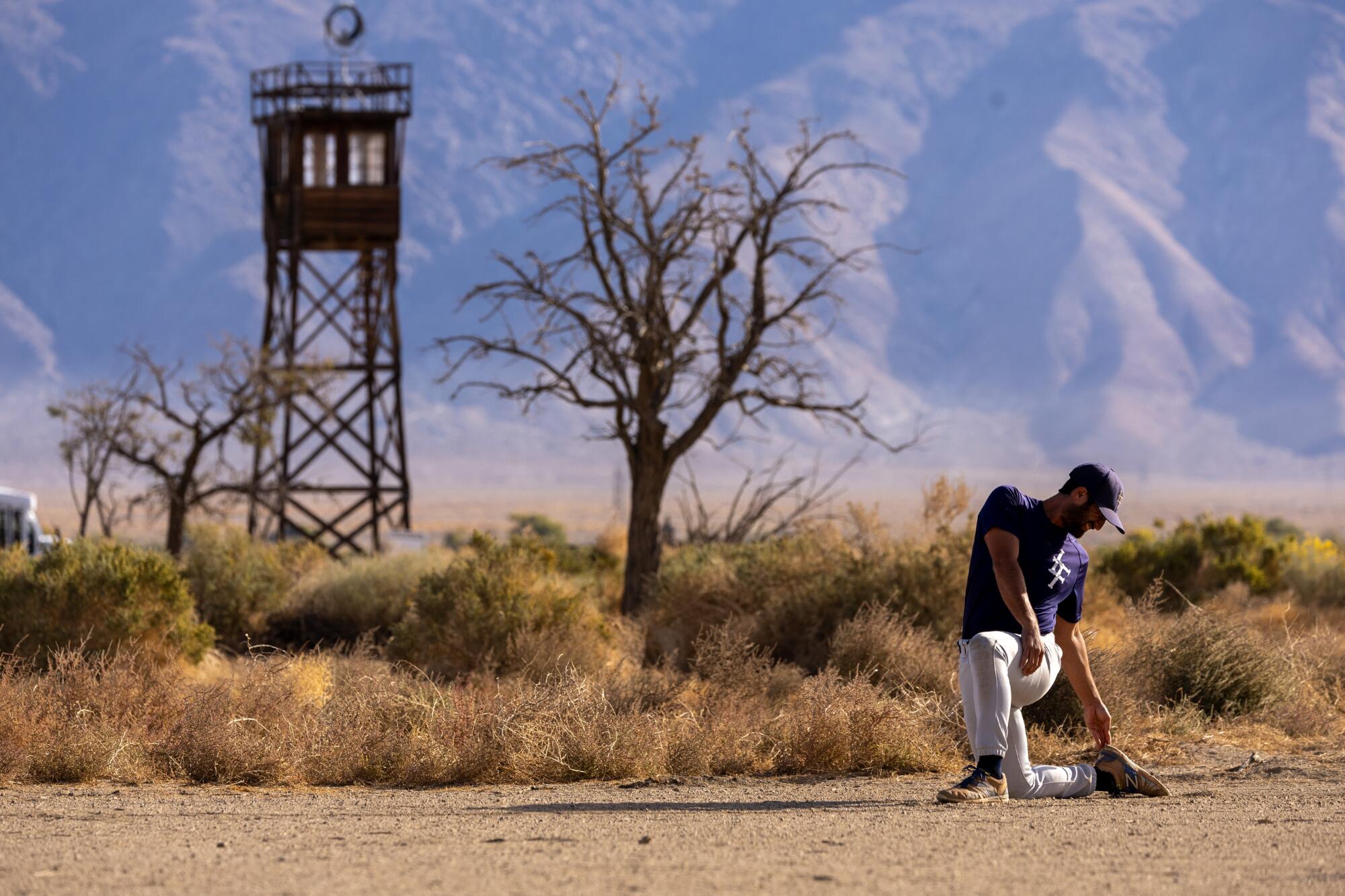 A player stretches at the restored baseball field at Manzanar with the watch tower looming in the background.