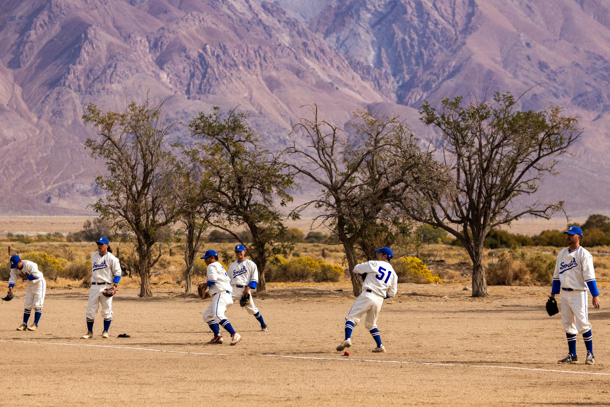 Players warm up before Saturday's game on the baseball field at Manzanar, restored to its wartime configuration.