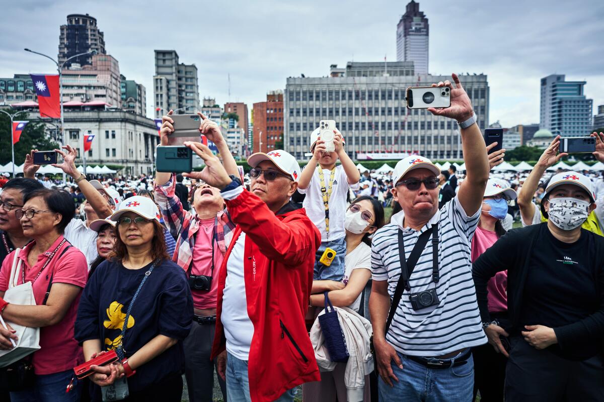 A crowd outside in an urban area, with many people holding up cellphones. 