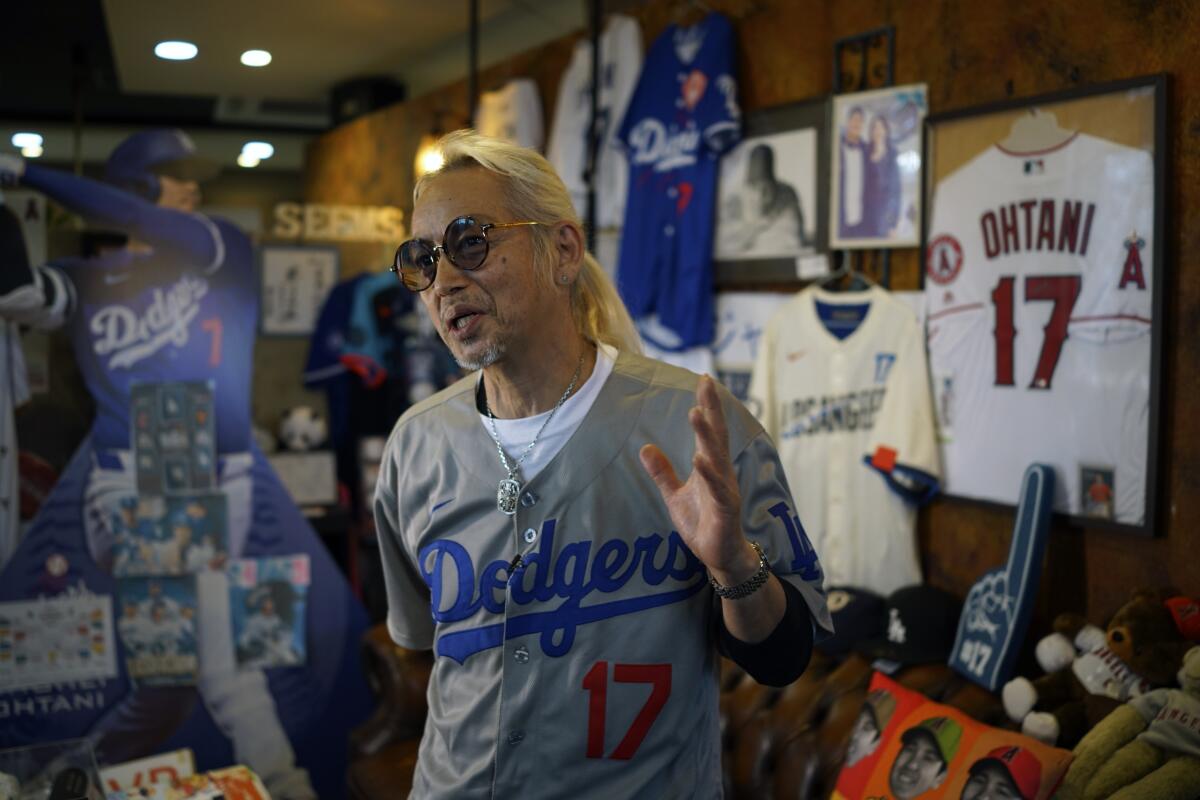 A man with a long blond ponytail and wearing a Dodgers #17 jersey, stands amid Ohtani memorabilia.